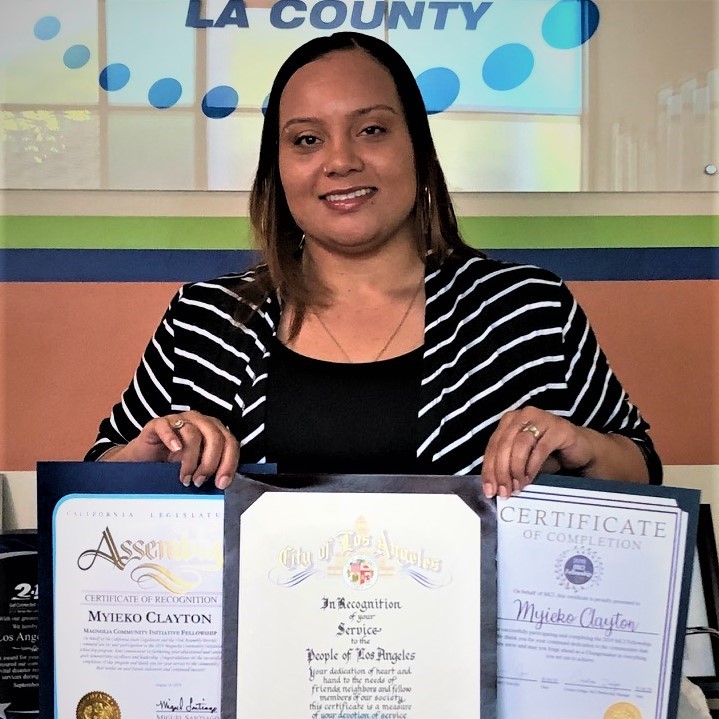 Myieko “Kiki” Clayton posing with certificates from the City of Los Angeles, California State Assembly, and Magnolia Community Initiative for successfully completing the MCI Fellowship program in 2019