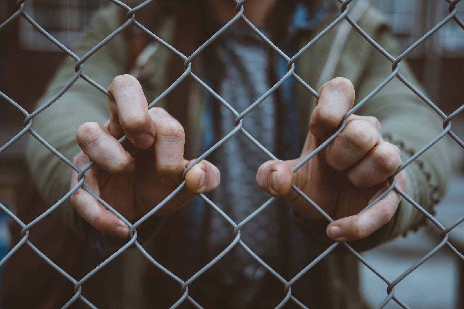 person grabbing onto fence with both hands with a blurred background