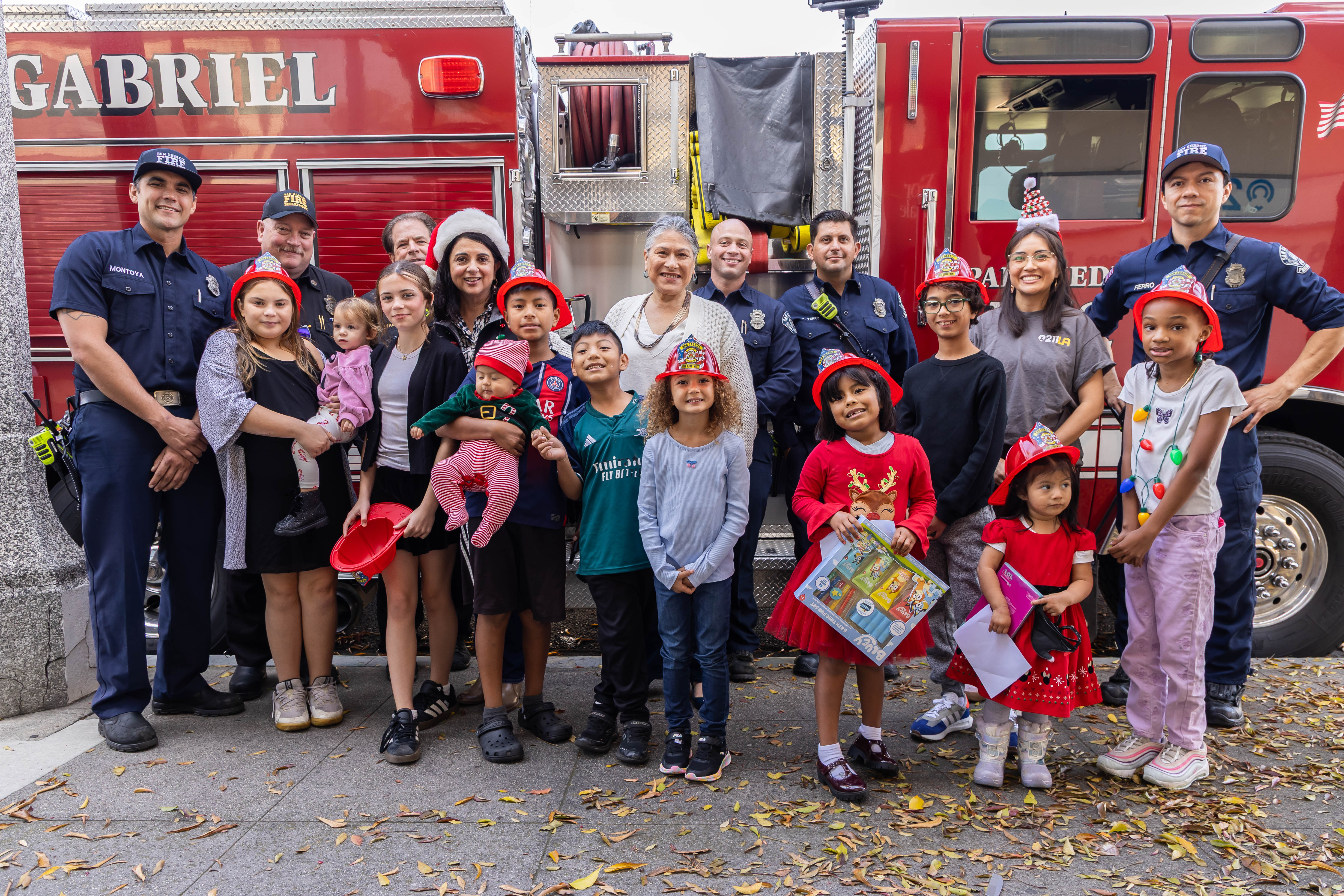 211 LA team with children and firefighters posing in front of a fire truck while some are holding gifts 
