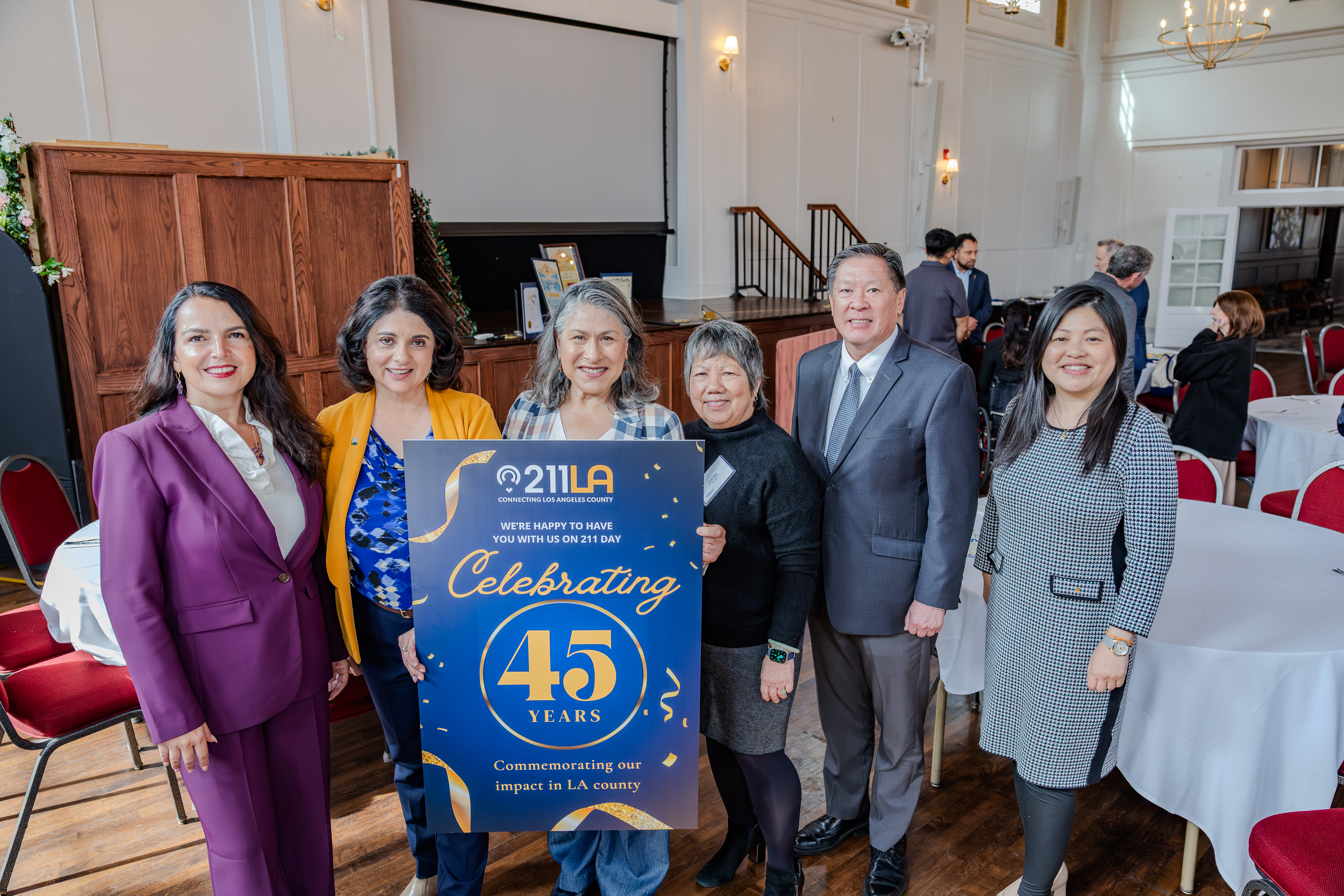 Maribel in the center holding the designed celebratory 211 LA sign that commemorates 211 LA's impact in the LA County. accompanied by others to the left and right side of her.