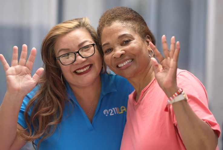 Care Coordinator left hand side, Yvonne wearing glasses and blue 211 LA shirt, Robin Ivory on the right, smiling and waving wearing a pink shirt