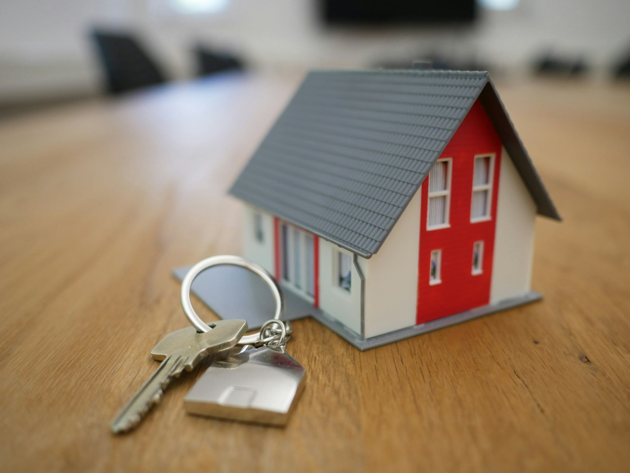 Miniaturized house on a brown table with a set of keys next to the house.