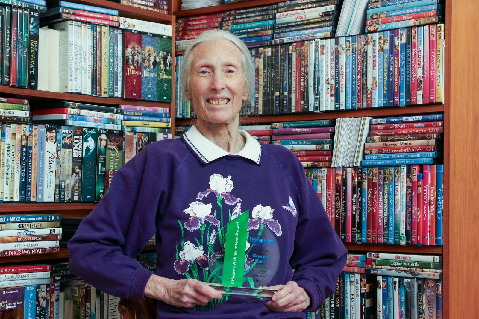 Georgia Sales poses in front of her cherished physical media collection with her 2024 Lifetime Achievement Award from Inform USA.