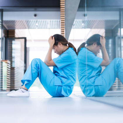Person in scrubs sitting on ground with hands to head 