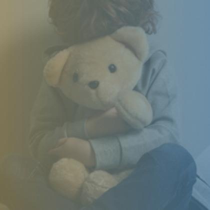 Child holding a teddy bear face is covered by the teddy bear, with a blue and yellow translucent color on the photo