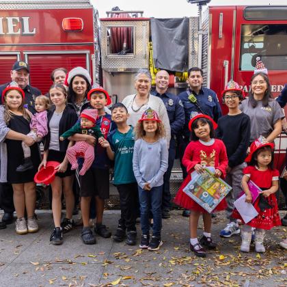 211 LA team with children and firefighters posing in front of a fire truck while some are holding gifts 