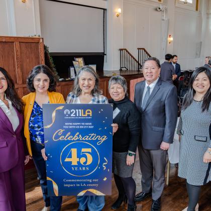 Maribel in the center holding the designed celebratory 211 LA sign that commemorates 211 LA's impact in the LA County. accompanied by others to the left and right side of her.