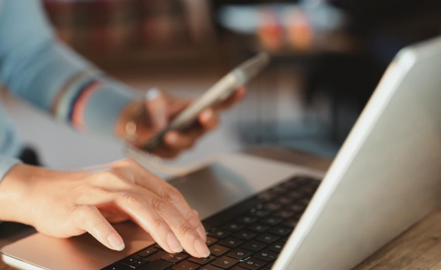 person typing on the computer while holding a smartphone