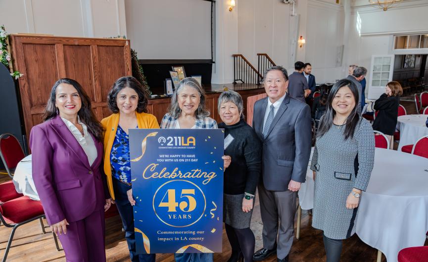 Executive Director, Maribel Marin, holding sign  that emphasizes the the commemoration of 211 LA's impact in the LA County, accompanied by others on both left and right side of her.