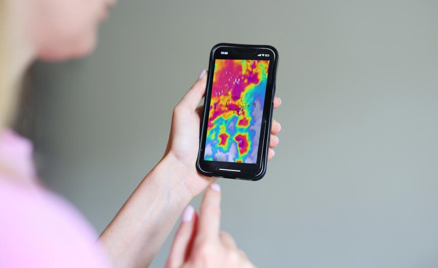 A person holding a smartphone displaying a colorful weather radar map.