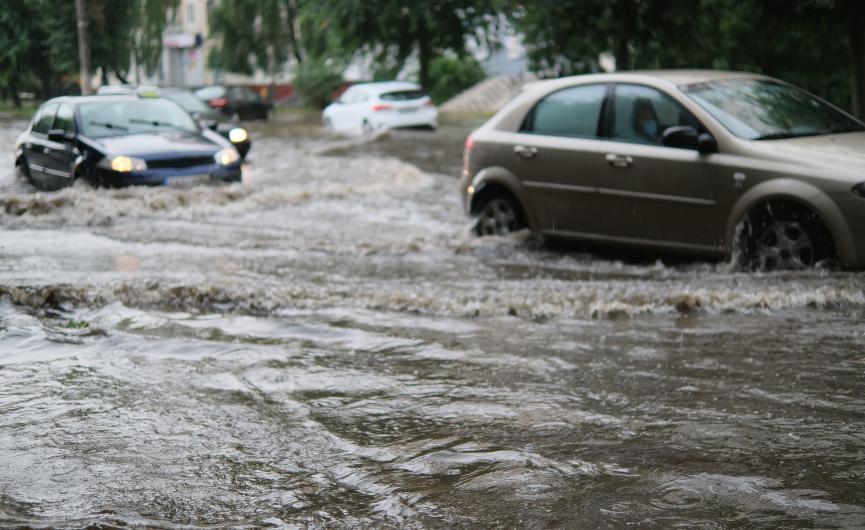 Cars driving through deep floodwater on a street.
