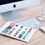 ipad with social media icons displayed on table with mac desktop