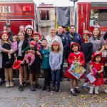 211 LA team with children and firefighters posing in front of a fire truck while some are holding gifts 