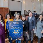 Maribel in the center holding the designed celebratory 211 LA sign that commemorates 211 LA's impact in the LA County. accompanied by others to the left and right side of her.