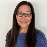A headshot picture of Suzanne Osimo, wearing a blue sweater and glasses with long brown hair