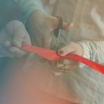Close-up of two people's hands participating in a ribbon-cutting ceremony, with one person holding a red ribbon taut while the other cuts it with a pair of scissors.