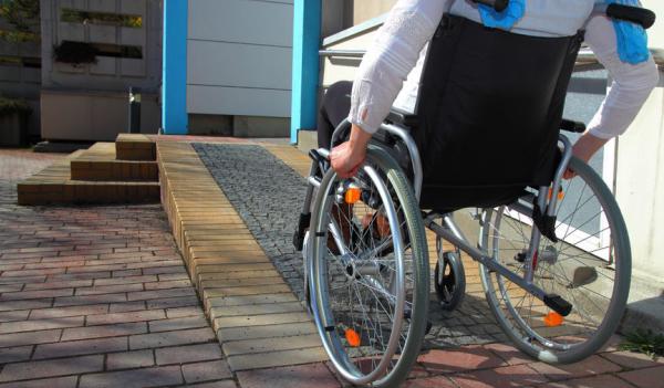 Image of person rolling wheelchair up ramp to house