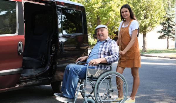 Image of senior man in wheelchair being helped into van, representing senior transportation services